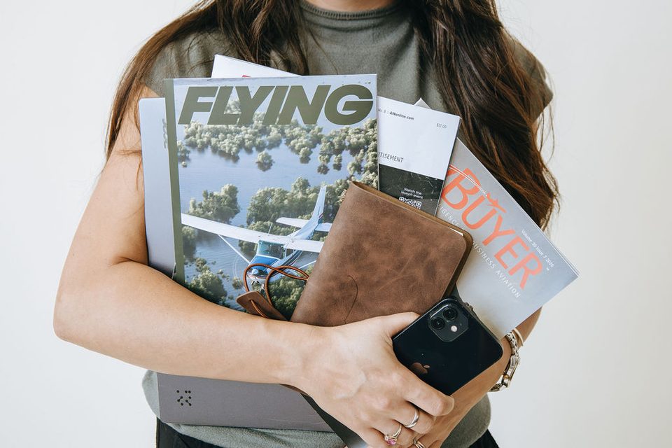 Arms full of aviation magazines, a planner, and a phone