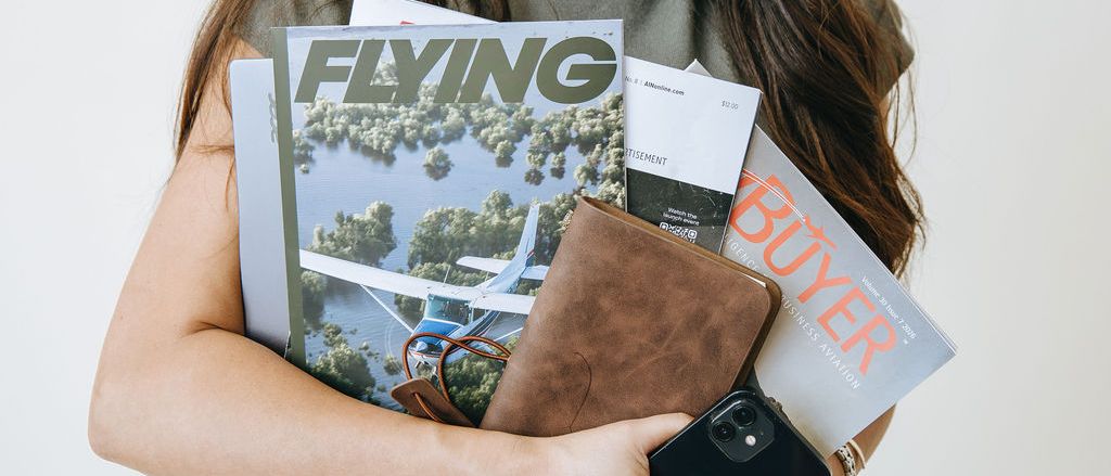 Arms full of aviation magazines, a planner, and a phone