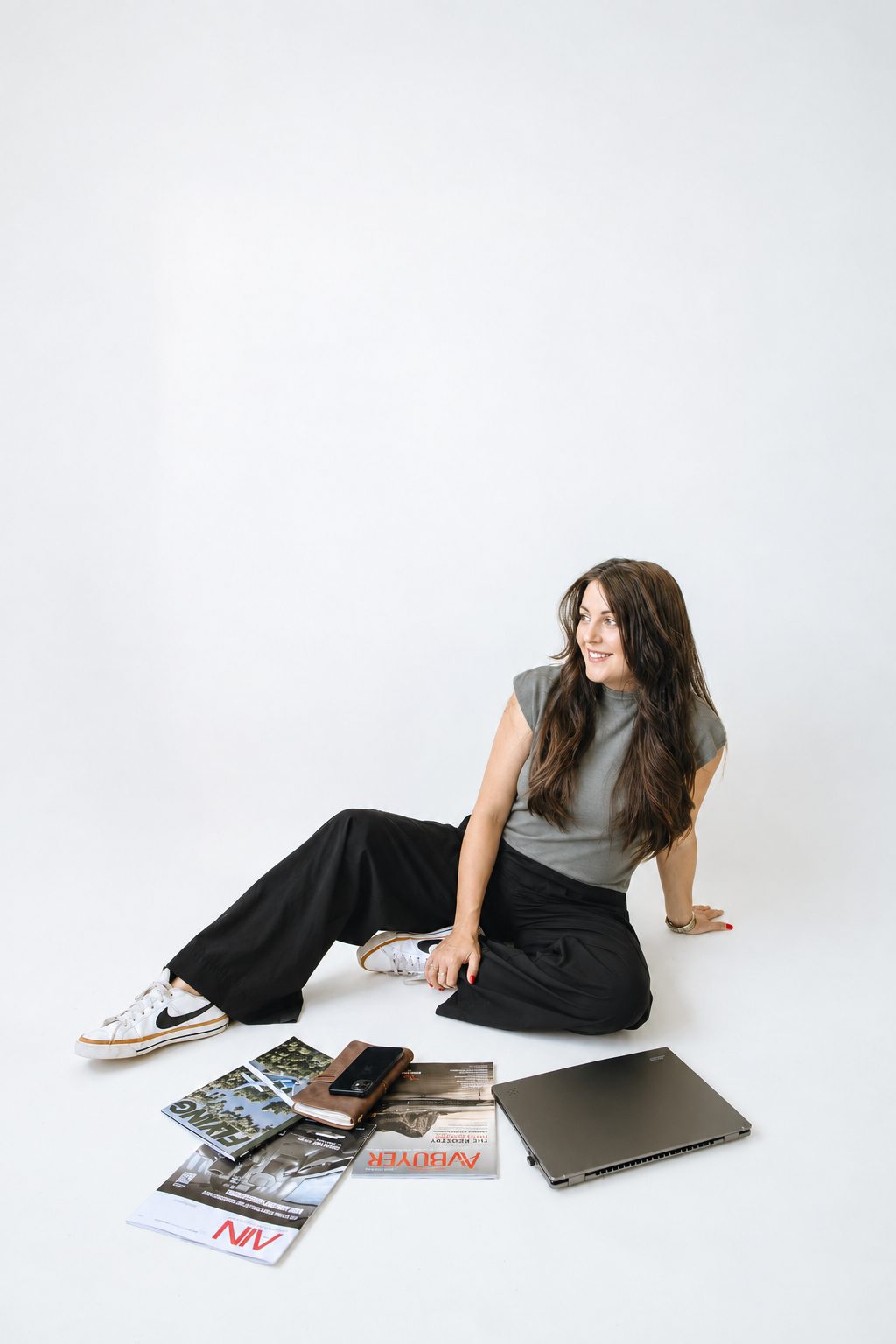 Emily seated on a white studio floor with aviation magazines and a laptop