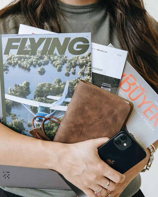 Arms full of aviation magazines, a planner, and a phone