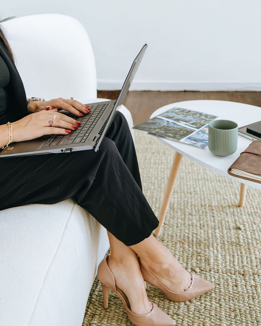 Hands typing on a laptop beside a coffee table with a phone, a mug, and a notebook
