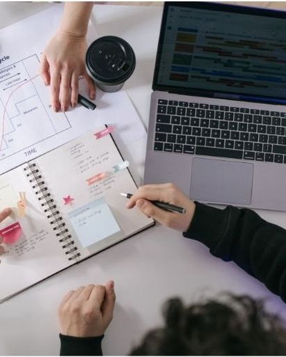 A team working through a plan together with a laptop, notebook, and printed chart