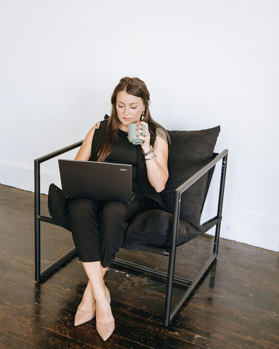 Emily in a black lounge chair with a laptop and a coffee mug
