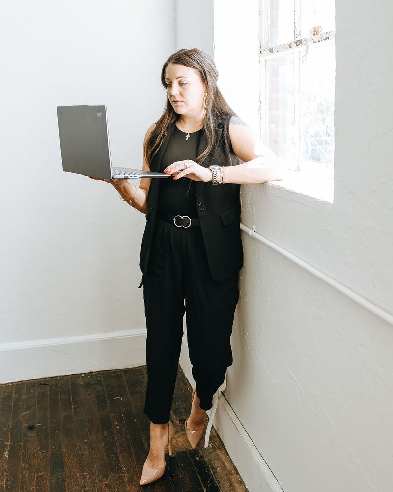 Emily standing by a tall window, reviewing a site on her laptop