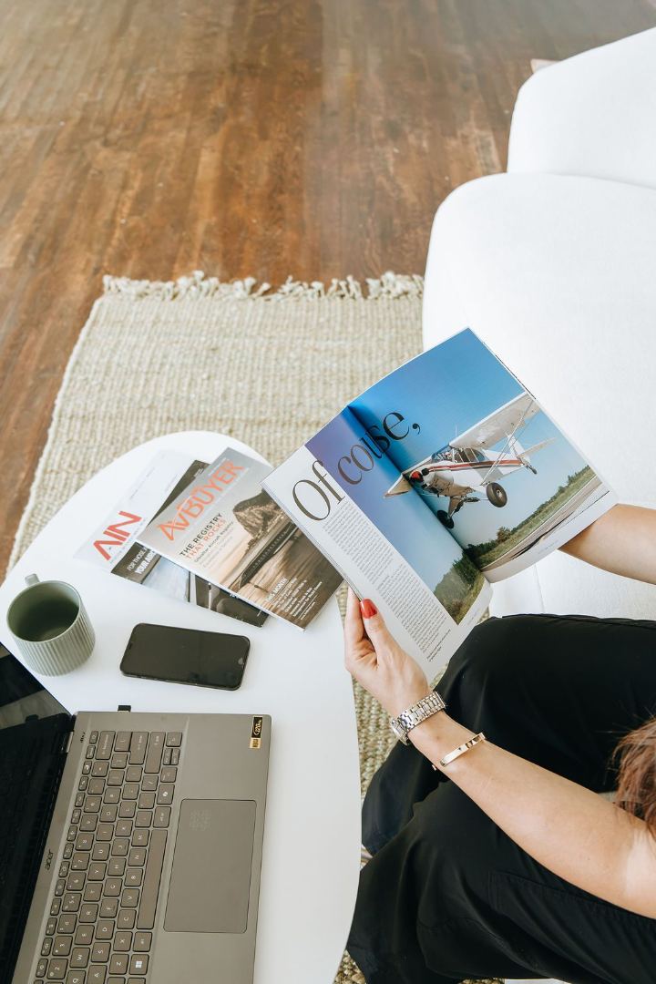 Overhead view of Emily reading an aviation magazine spread beside AIN and AvBuyer